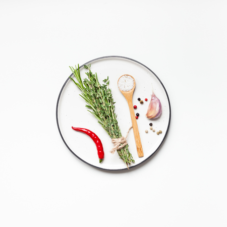 Flat lay overhead view empty plate mockup blank text space invitation card on white background with greens herbs and spices. Menu design food background with cooking ingredientsの写真素材