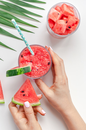 Creative scandinavian style flat lay top view of fresh watermelon slices smoothie drink in glass woman hands on white table background copy space. Minimal summer fruits concept for blog or recipe bookの写真素材