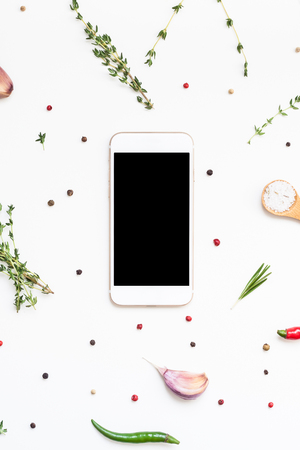 Flat lay overhead view smartphone mockup blank text space on white background with greens herbs and spices. Menu design food blog recipe cookbook or delivery app with cooking ingredientsの写真素材