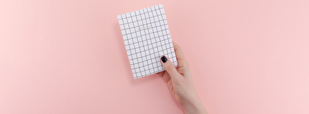 Top view of woman hand with stylish black manicure holding notepad with copy space on pink color paper background in minimal style. Template for feminine blog social mediaの写真素材