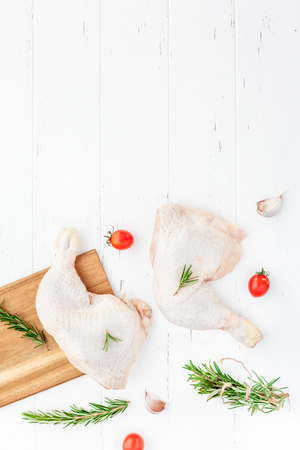Creative Top view flat lay of fresh raw chicken legs with rosemary herbs garlic tomatoes on white wooden background with copy space. Food preparation recipe cooking conceptの写真素材