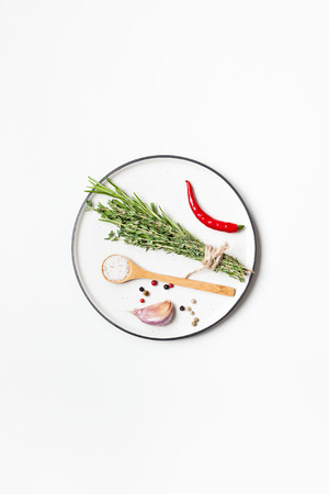 Flat lay overhead view empty plate mockup blank text space invitation card on white background with greens herbs and spices. Menu design food background with cooking ingredientsの写真素材