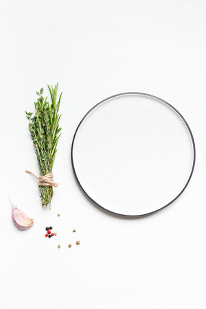 Flat lay overhead view empty plate mockup blank text space invitation card on white background with greens herbs and spices. Menu design food background with cooking ingredientsの写真素材