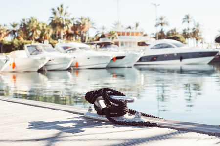 Mooring yacht rope with a knotted end tied around a cleat on a wooden pier against marina viewの写真素材