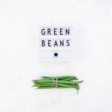 Creative scandinavian style flat lay top view of fresh green beans and text in lightbox on white concrete table background copy space. Minimal house cooking concept template for blog or recipe bookの写真素材