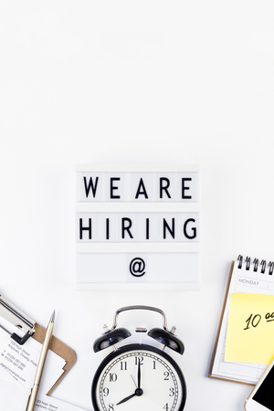 Creative top view flat lay of desk with we are hiring text on lightbox with copy space on white background in minimal style. Concept of new job, hiring recruitment process, new team members screeningの写真素材