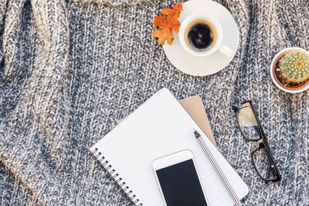 Creative autumn flat lay overhead top view stylish home workspace with smartphone notebook coffee cup cozy gray knitted plaid background copy space. Fall season template for feminine blog social mediaの写真素材