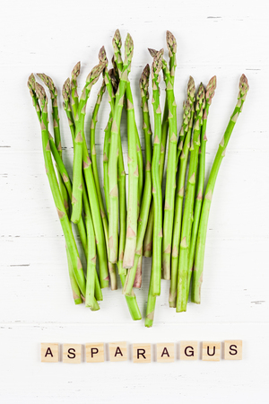 Creative scandinavian style flat lay top view mockup of fresh green asparagus on white wooden table background copy space. Minimal house cooking concept mock up for blog or recipe bookの写真素材