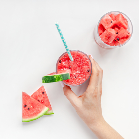Creative scandinavian style flat lay top view of fresh watermelon slices smoothie drink in glass woman hands on white table background copy space. Minimal summer fruits concept for blog or recipe bookの写真素材