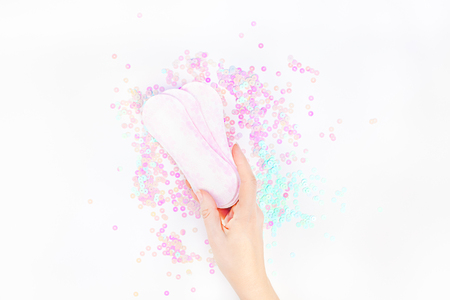 Woman hand holding daily sanitary napkins on white background and pearl pastel confetti sparkles with copy space. Creative female healthcare concept top view flat lay for your blog, text or designの写真素材
