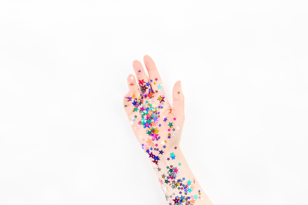 Bright festive color confetti star sparkles with woman hand on white background. Creative conceptual Christmas holiday birthday party top view flat lay backdrop for your blog, text or designの写真素材