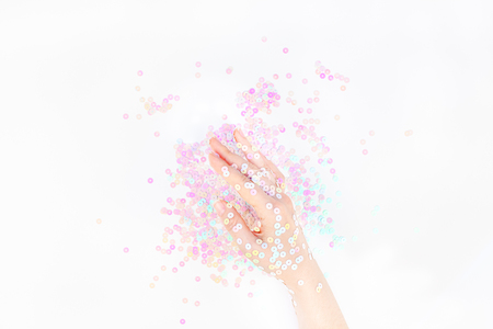 Pearl pastel confetti sparkles with woman hand on white background. Creative conceptual top view flat lay backdrop for your blog, text or designの写真素材