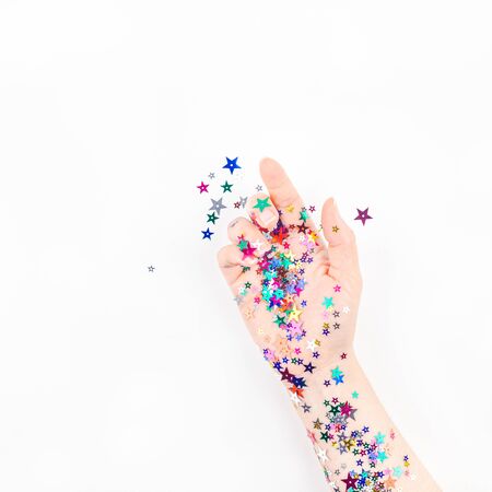 Bright festive color confetti star sparkles with woman hand on white background. Creative conceptual Christmas holiday birthday party top view flat lay backdrop for your blog, text or designの写真素材