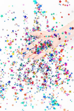 Bright festive color confetti star sparkles with woman hand on white background. Creative conceptual Christmas holiday birthday party top view flat lay backdrop for your blog, text or designの写真素材