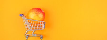 Mango fruit in shopping cart in creative conceptual top view flat lay composition isolated on bold orange color background in minimal style with copy space. Pop art posterの写真素材