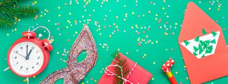 New Year or Christmas pattern flat lay top view with red alarm clock twelve midnight fir tree branch Xmas holiday celebration green paper bright colorful confetti background. Long wide banner 2020の写真素材