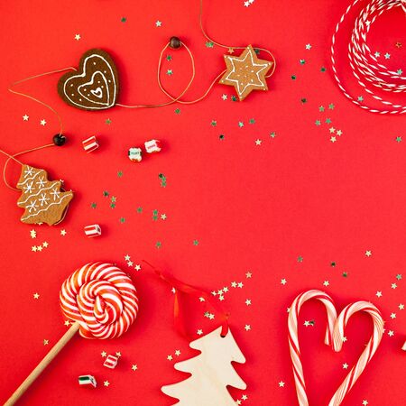 New Year or Christmas decoration flat lay top view Xmas holiday celebration handmade decor wooden toys sweets golden stars glitter on red paper background. Square template frame greeting card designの写真素材