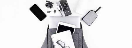 Creative top view flat lay of open backpack with laptop and tablet inside, mobile phone, copy space white background minimal style. Concept of modern man accessories for education, business and lifeの写真素材