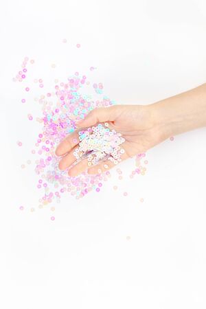 Pearl pastel confetti sparkles with woman hand on white background. Creative conceptual top view flat lay backdrop for your blog, text or designの写真素材