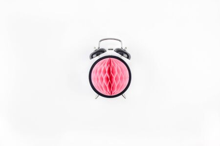 Birthday or baby shower party invitation card template. Black alarm clock with pink honeycomb paper ball on white background. Creative conceptual top view flat lay composition in minimal styleの写真素材