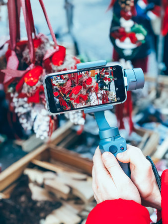 GERMANY, NUREMBERG - DECEMBER 17, 2018: Close-up of man blogger hands shooting video on smartphone IPhoneXS using an image stabilizer DJI Osmo Mobile on the Christmas market in Nurembergのeditorial素材