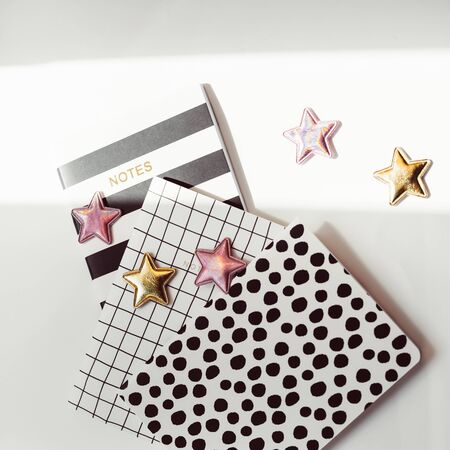 Desktop feminine composition with patterned notepads, golden stars and deer clips on white table with sun light and shadows. Top view flat lay concept for bloggerの写真素材