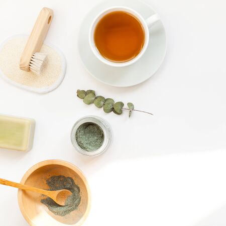 Spa, beauty cosmetics and body care treatment concept with copy space. Creative top view flat lay composition with cup of tea, green spirulina cleansing mask in wooden bowl on white backgroundの写真素材