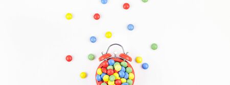 Birthday party invitation card template. Red alarm clock with multicolor candies on white background. Creative conceptual top view flat lay composition in minimal styleの写真素材