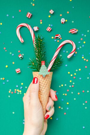 New Year Christmas Xmas holiday celebration woman hand red manicure holding waffle cone candy canes fir tree branch copy space green color paper background. Template greeting card 2020の写真素材