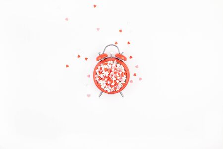 Valentine's Day. Creative holiday concept made from red heart shaped sweet confetti with alarm clock. Valentines day top view love composition on white background.の写真素材