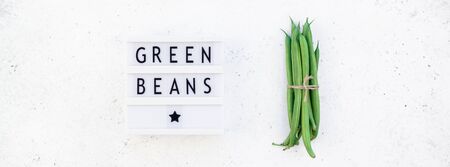 Creative style flat lay top view of fresh green beans and text in light box on white concrete table...