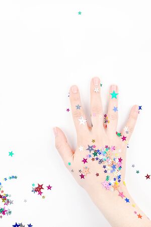 Bright festive color confetti star sparkles with woman hand on white background. Creative conceptual Christmas holiday birthday party top view flat lay backdrop for your blog, text or designの写真素材
