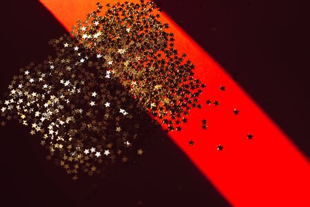 Holiday composition. New Year or Christmas pattern flat lay top view Xmas holiday celebration with golden stars confetti decoration on deep red background with copy space harsh natural sunlight shadowの写真素材