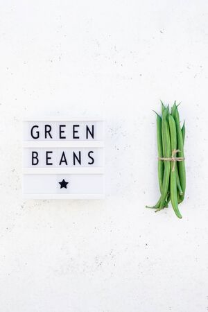 Creative scandinavian style flat lay top view of fresh green beans and text in lightbox on white concrete table background copy space. Minimal house cooking concept template for blog or recipe bookの写真素材