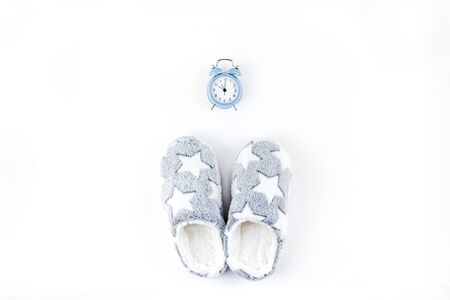 Sleep. Soft fluffy slippers and blue alarm clock isolated on white background. Creative conceptual top view flat lay in minimal style. Rest, good night, insomnia, relaxation, tired, hygge conceptの写真素材