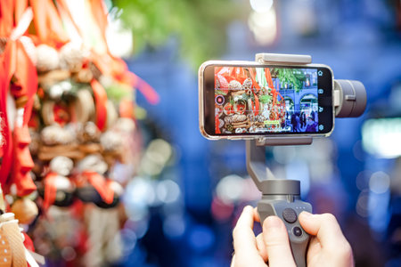 GERMANY, MUNICH - DECEMBER 20, 2018: Close-up of man blogger hands shooting video on smartphone IPhoneXS using an image stabilizer DJI Osmo Mobile on the Christmas market in Munichのeditorial素材