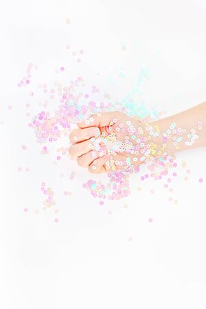 Pearl pastel confetti sparkles with woman hand on white background. Creative conceptual top view flat lay backdrop for your blog, text or designの写真素材