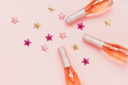 Christmas or New Year composition with bottles of rose champagne and golden shiny sparkle star confetti on pastel pink background, top view. Celebration flat lay. Party creative conceptの写真素材