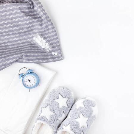 Sleep. Fluffy slippers, bottle with pills and blue alarm clock isolated on white background. Creative conceptual top view flat lay minimal style. Rest, good night, insomnia, relaxation, tired conceptの写真素材