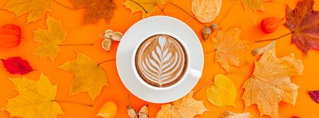 Autumn flat lay composition with dry leaves wreath frame and coffee latte cup on bold orange color...