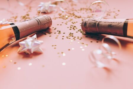 Christmas or New Year composition with bottles of rose champagne and golden shiny sparkle star confetti on pastel pink background, side view. Party Celebration creative conceptの写真素材