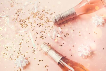 Christmas or New Year composition with bottles of rose champagne and golden shiny sparkle star confetti on pastel pink background, top view. Celebration flat lay. Party creative conceptの写真素材