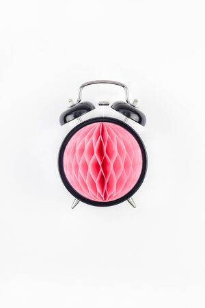 Birthday or baby shower party invitation card template. Black alarm clock with pink honeycomb paper ball on white background. Creative conceptual top view flat lay composition in minimal styleの写真素材