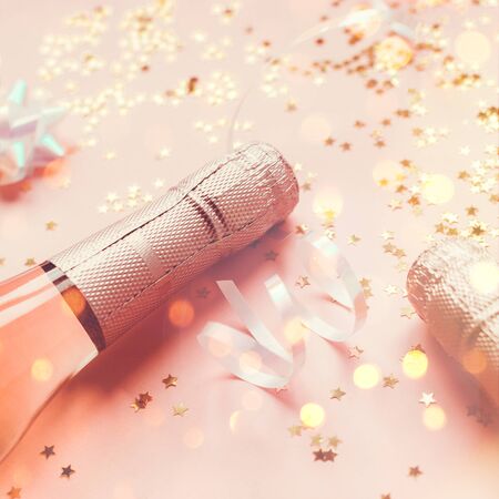 Christmas or New Year composition with bottles of rose champagne and golden shiny sparkle star confetti on pastel pink background, side view. Party Celebration creative conceptの写真素材
