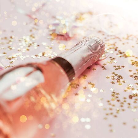 Christmas or New Year composition with bottles of rose champagne and golden shiny sparkle star confetti on pastel pink background, side view. Party Celebration creative conceptの写真素材