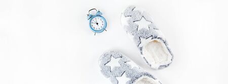 Sleep. Soft fluffy slippers and blue alarm clock isolated on white background. Creative conceptual top view flat lay in minimal style.の写真素材