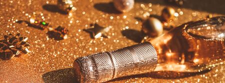 Christmas or New Year composition with bottle of rose champagne and golden sparkling decoration on golden shiny background, side view with festive bokeh and shadows. Party Celebration creative conceptの写真素材