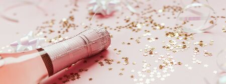 Christmas or New Year composition with bottles of rose champagne and golden shiny sparkle star confetti on pastel pink background, side view. Party Celebration creative conceptの写真素材