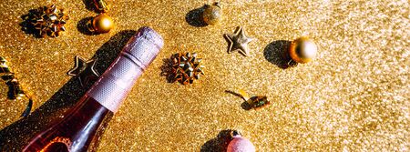 Christmas or New Year composition with bottle of rose champagne and golden sparkling decoration on golden shiny background, top view with festive bokeh and shadows. Party Celebration creative conceptの写真素材