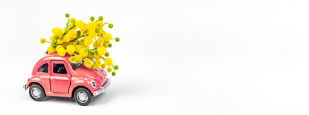Moscow, Russia - February 23, 2019: 8 March International Women's Day card with toy model retro car delivering bouquet of mimosa flowers on white background. Valentine's day, Flower delivery conceptのeditorial素材